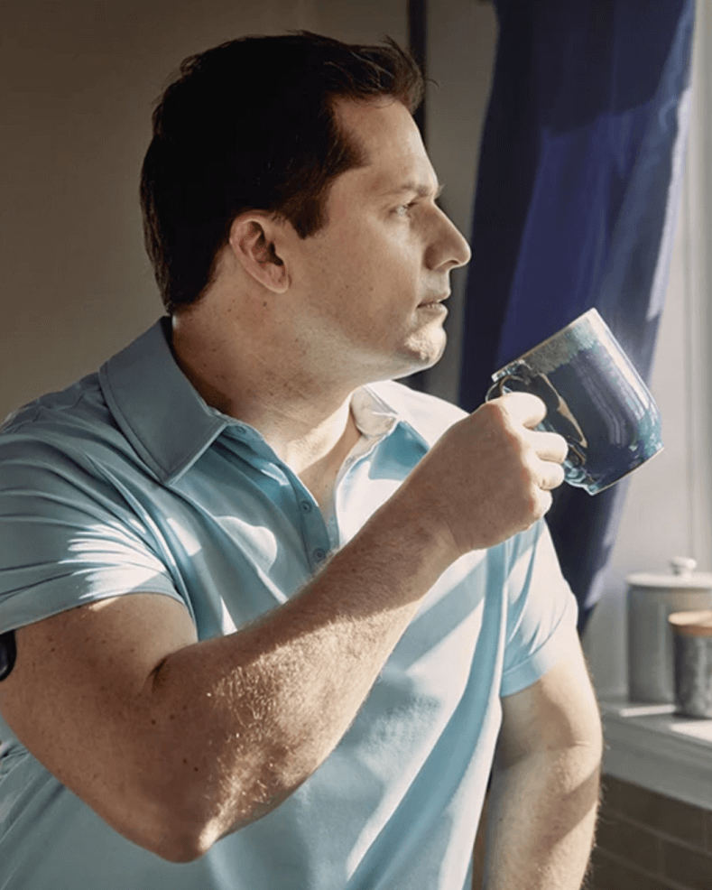 Ein Eversense CGM Benutzer, der eine blaue Tasse hält und den Eversense Smart Transmitter am Arm trägt.