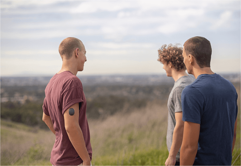 3 Freunde stehen draußen auf einem Feld, einer trägt einen Eversense CGM Transmitter.