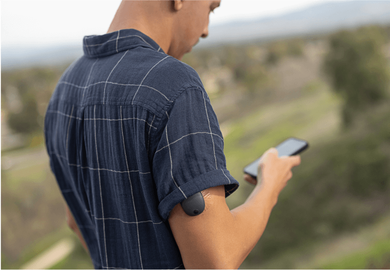 Eversense Benutzer steht im Freien und verwendet ein Smartphone zur Überwachung seines Glukosespiegels.