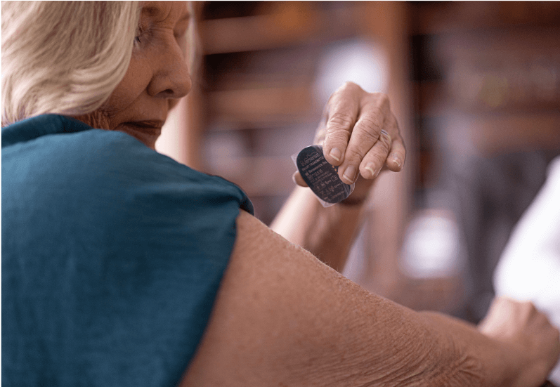 Eversense Benutzerin bringt den Eversense 365 Smart Transmitter in einer gemütlichen Umgebung zu Hause am Oberarm an. 