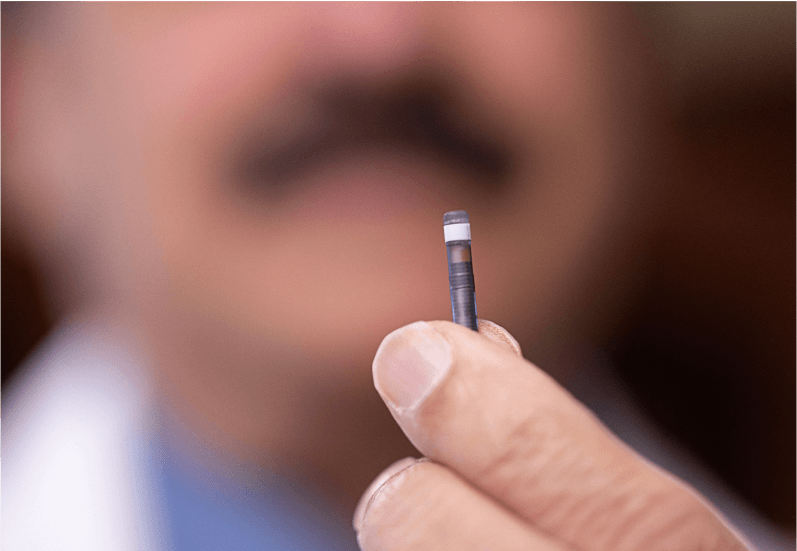 Eine Nahaufnahme des kleinen Eversense Sensors, der zwischen 2 Fingern gehalten wird.