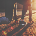 Person in Startposition hockend, mit Sportschuhen, auf einer sonnenbeschienenen Straße, die sich auf das Laufen vorbereitet.