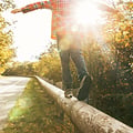 Ein Kind, das mit ausgestreckten Armen auf einem Holzgeländer balanciert, während das Sonnenlicht durch die Bäume entlang einer ruhigen Straße scheint.