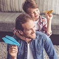 Ein Eversense CGM Benutzer hält lächelnd einen blauen Papierflieger, während ein Kind auf seinem Rücken einen gelben Papierflieger hält.